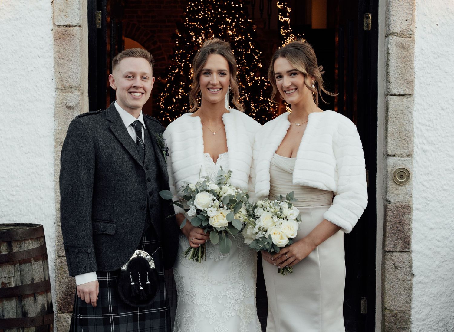 Formal wedding party members posing by stone archway with twinkle lights in background.