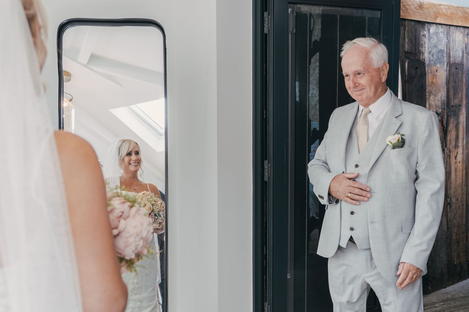 A bride and groom share an emotional first look moment in a rustic wooden doorway.
