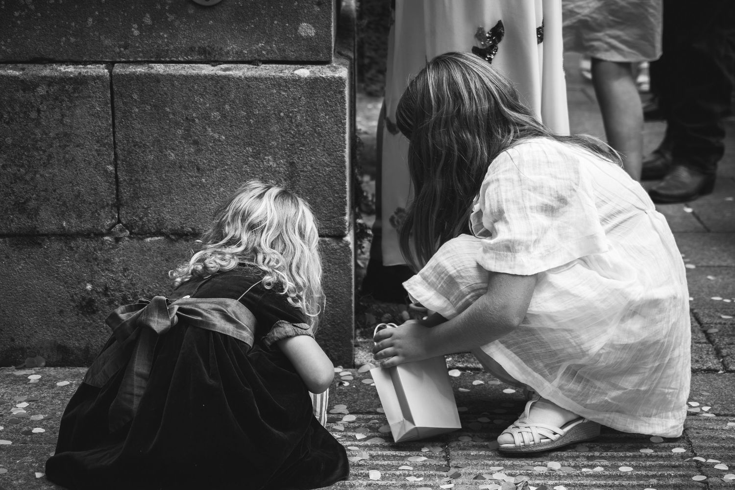 Children play together while sitting on the ground in a candid black and white photograph.