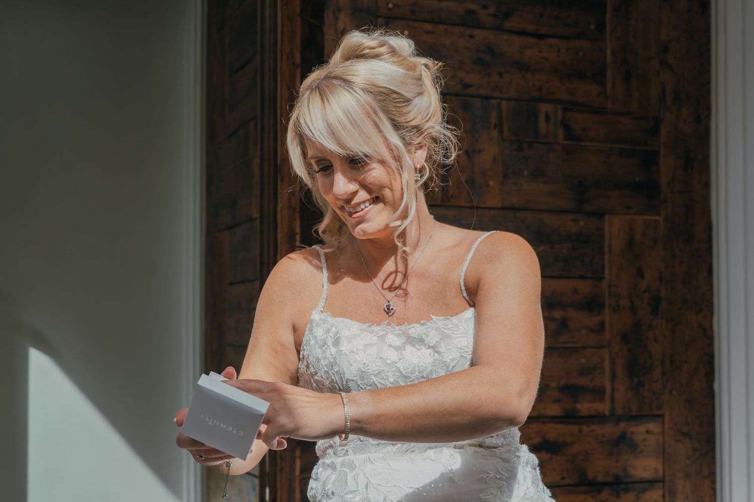 A person in a white wedding dress stands in an elegant doorway with exposed brick walls and natural lighting.