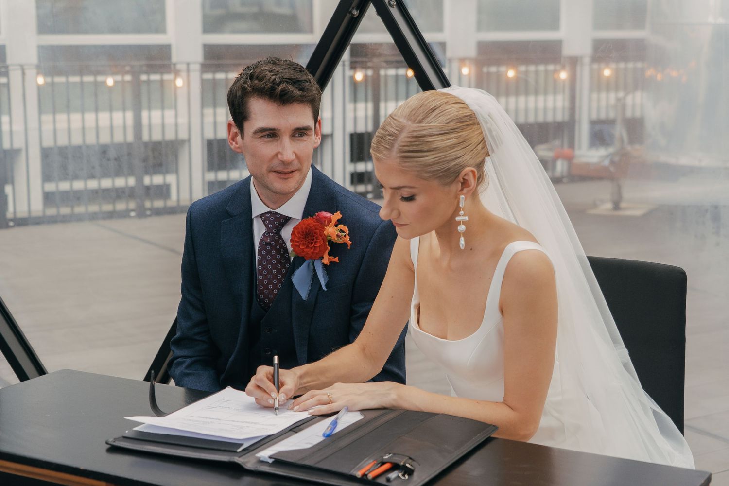 A newly married couple signs marriage documents with their officiant at a ceremony table.