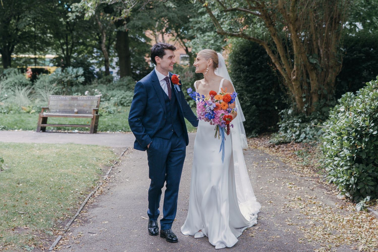 A happy couple walks along a garden path while sharing a joyful moment together on their wedding day.