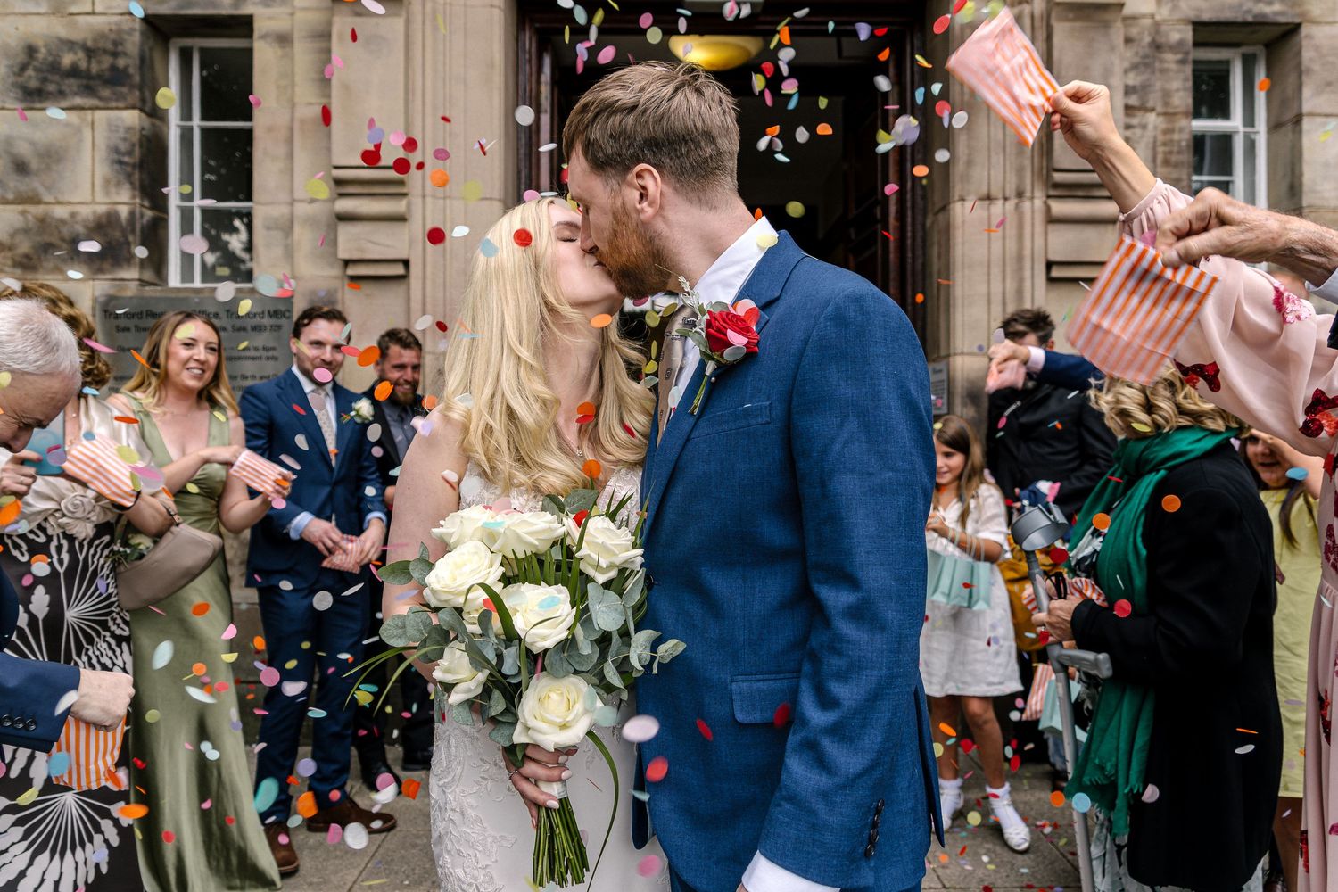 Wedding guests shower the happy couple with colorful confetti outside a stone building during a joyful celebration.