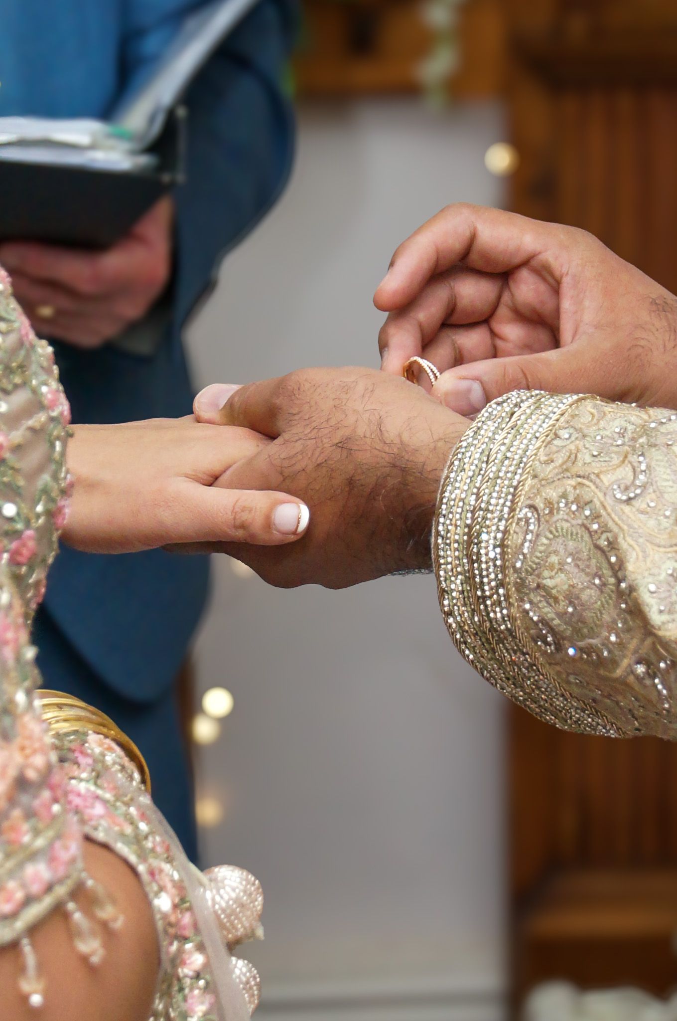 Hands adorned in glittering traditional wedding attire exchange rings during an elegant ceremony.