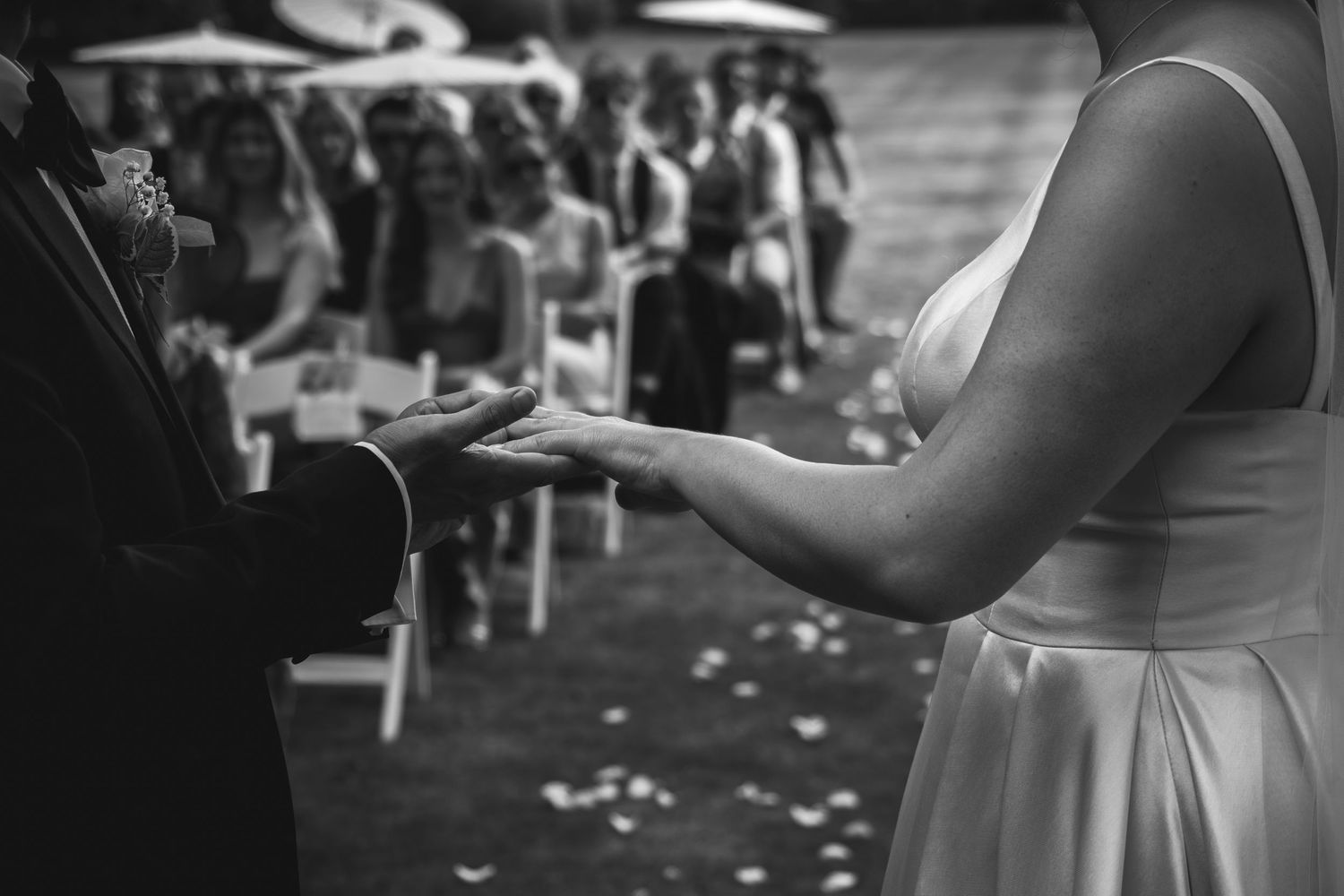 Close-up black and white shot of hands exchanging rings during an outdoor wedding ceremony.