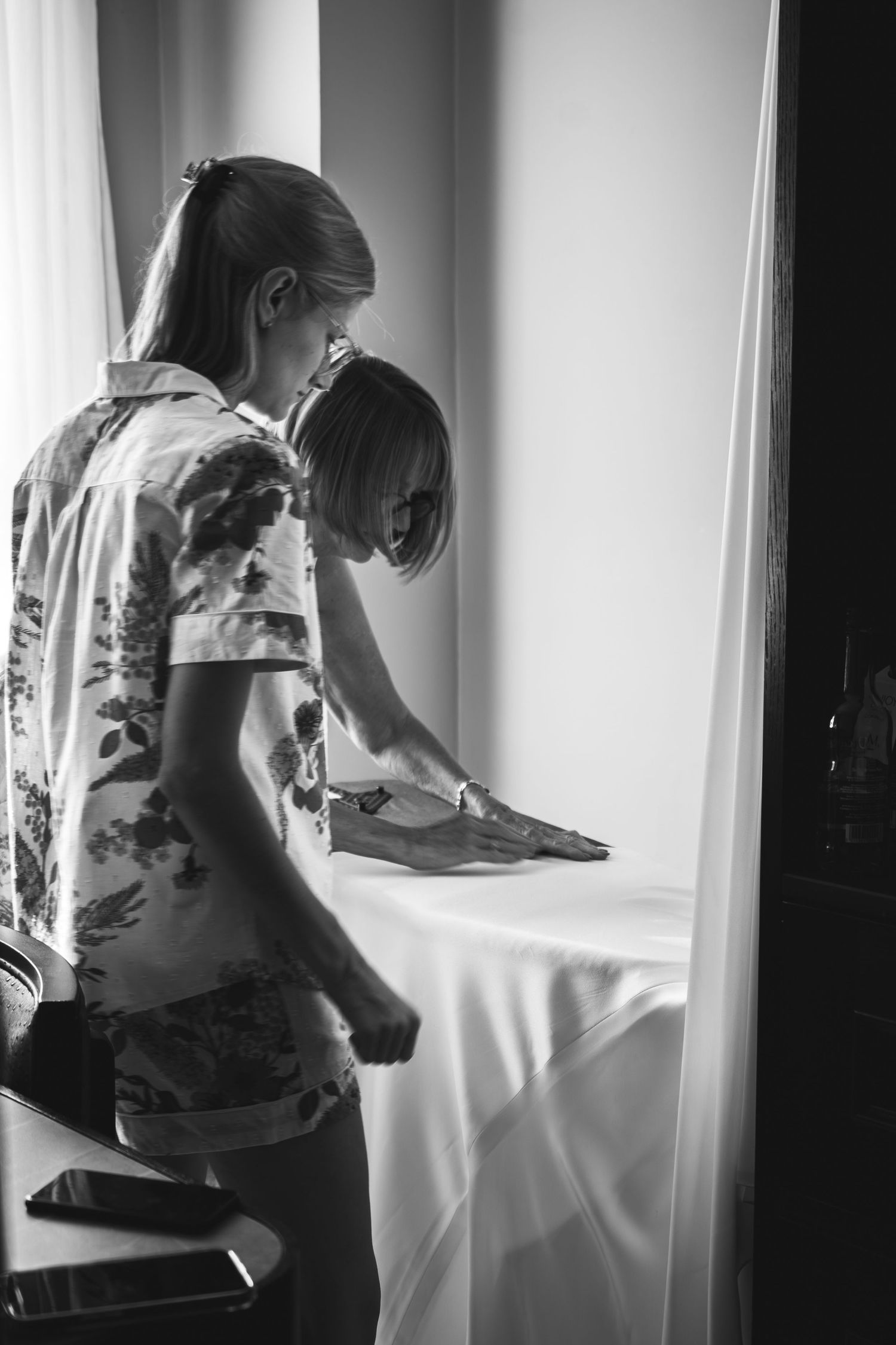 Two people in casual attire work together writing or drawing on white papers by a window in black and white photography.