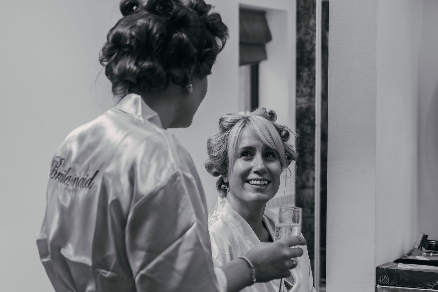 Bridesmaids and bride getting ready in white satin robes on the morning of a wedding event.