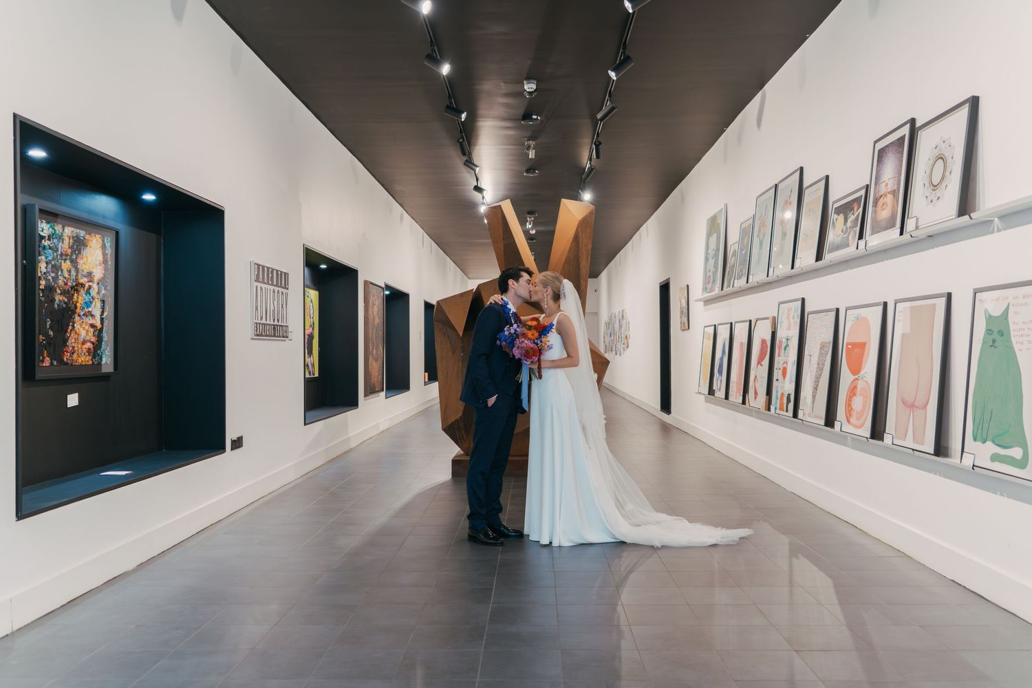 Art gallery visitors browse framed photographs displayed along white walls in a modern exhibition space.