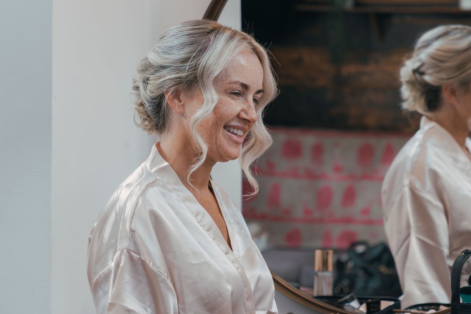 Women in matching white silk robes laugh and celebrate together during wedding preparations.