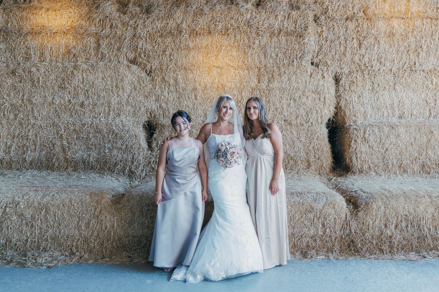 Wedding party standing in casual poses against a rustic barn wall with natural lighting.