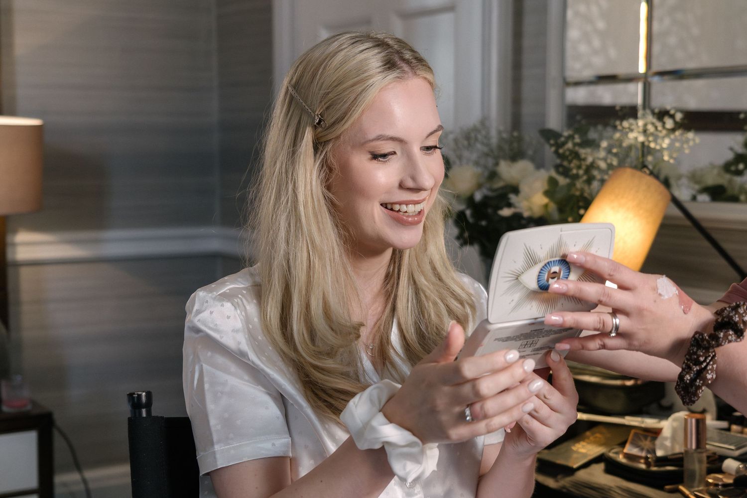 A person in a white t-shirt holds and lights a candle in a cozy indoor setting.