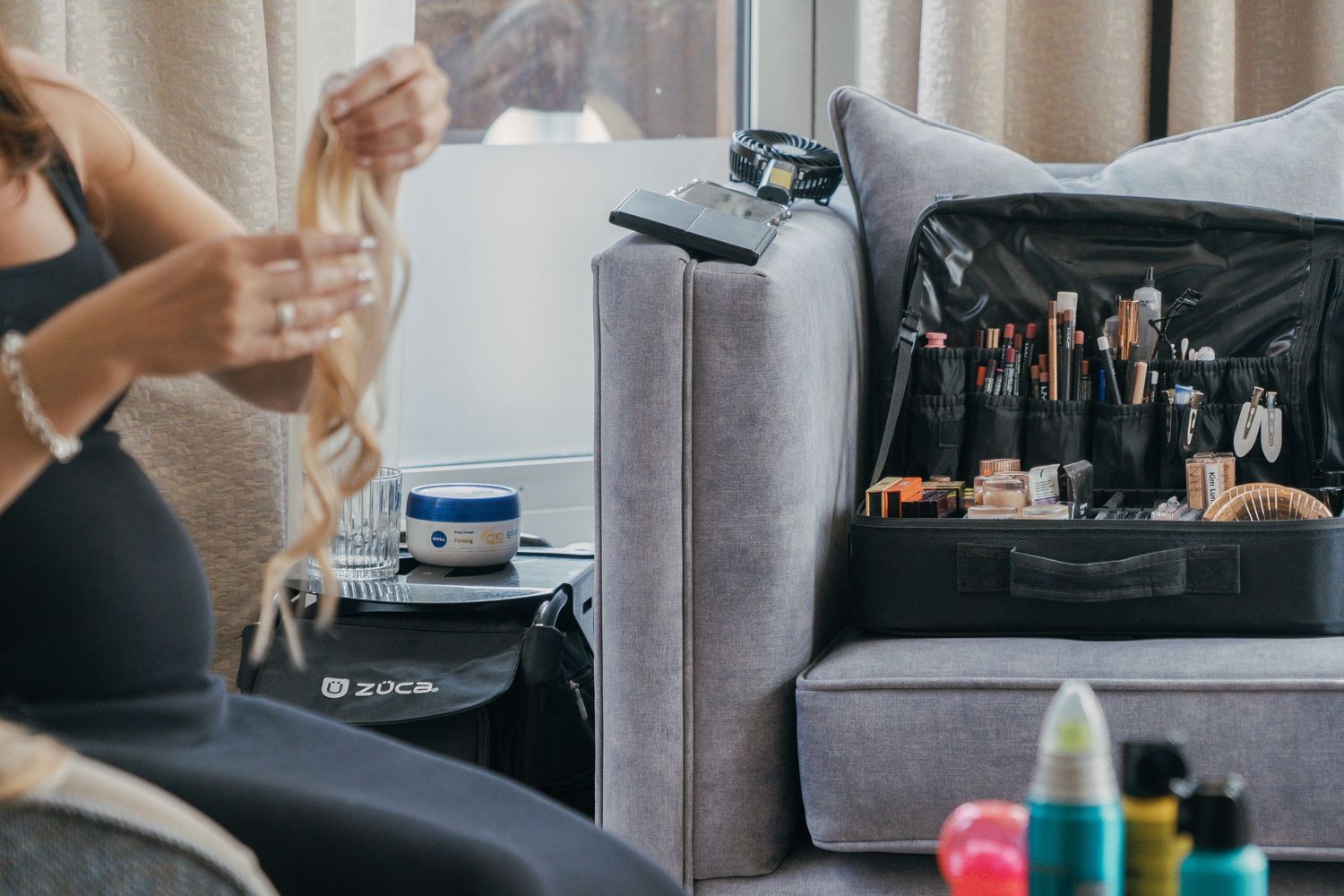 Professional makeup brushes and cosmetics arranged beside a gray sofa during a beauty preparation session.