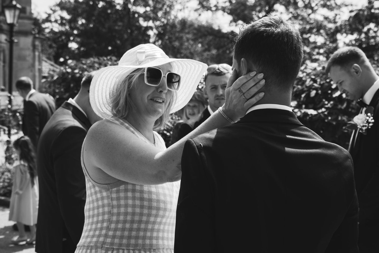 A guest in a summer hat and gingham dress greets others at an outdoor wedding.