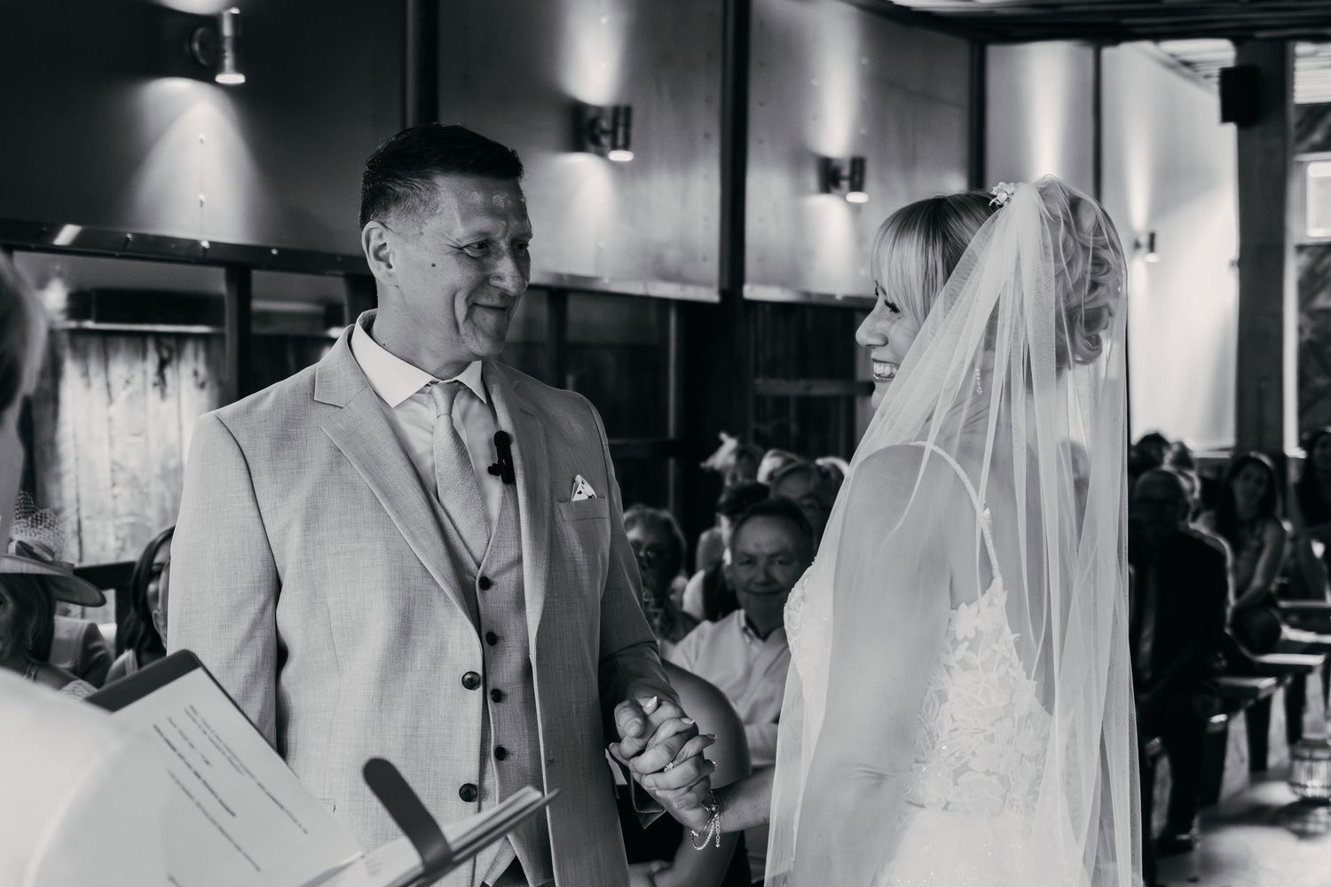 Black and white photo of wedding reception with guests gathering in dimly lit indoor venue.