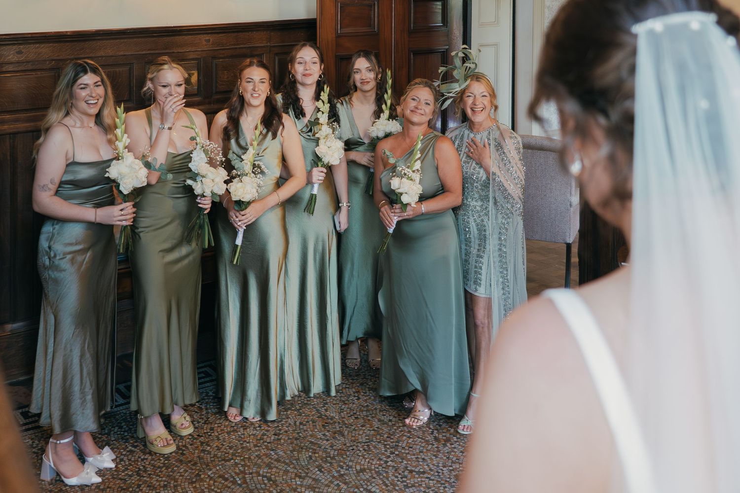 Wedding party in sage green bridesmaid dresses standing together in an emotional candid moment.