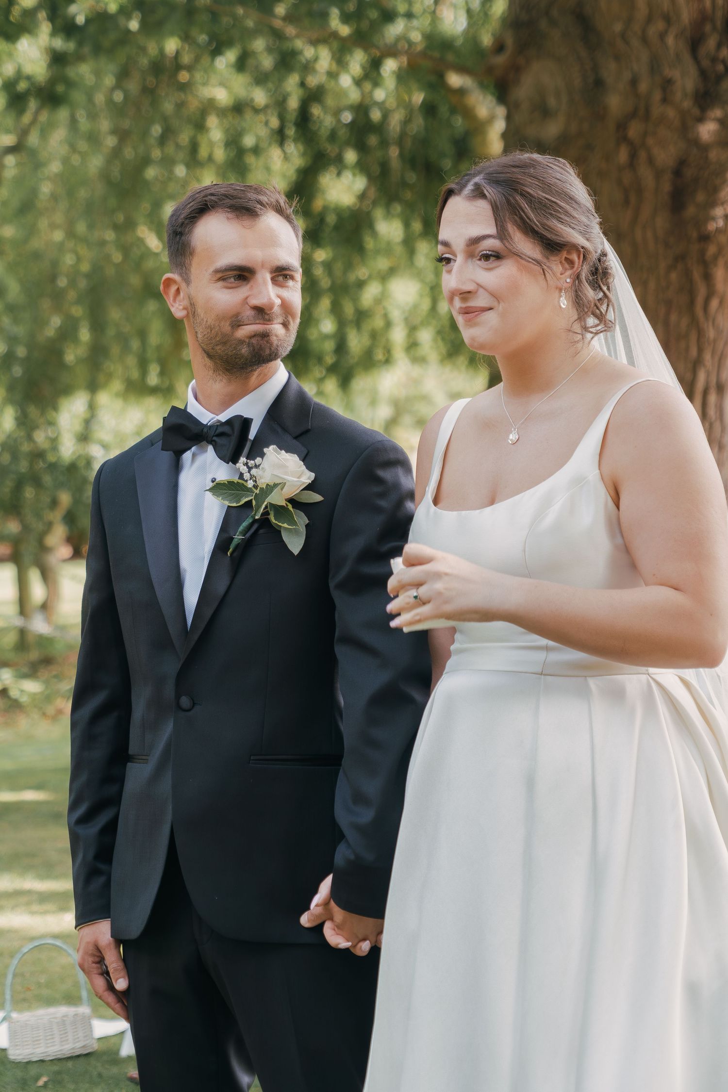 A couple shares a joyful moment during their outdoor wedding ceremony in a sunlit garden setting.