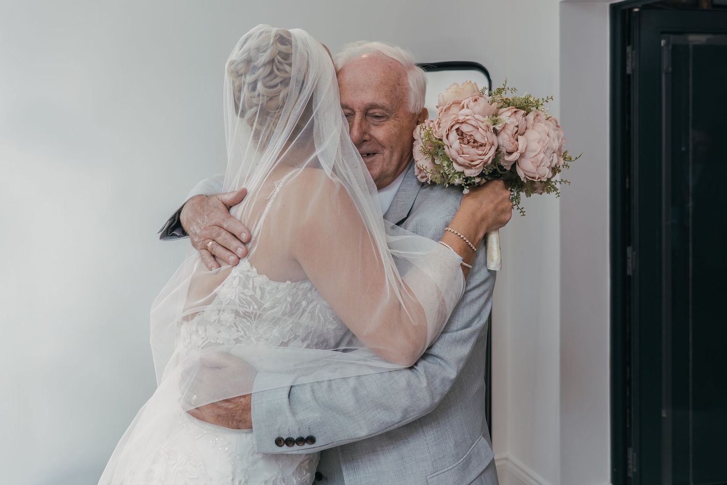 A touching moment between a bride and an elderly man sharing an emotional embrace at a wedding celebration.
