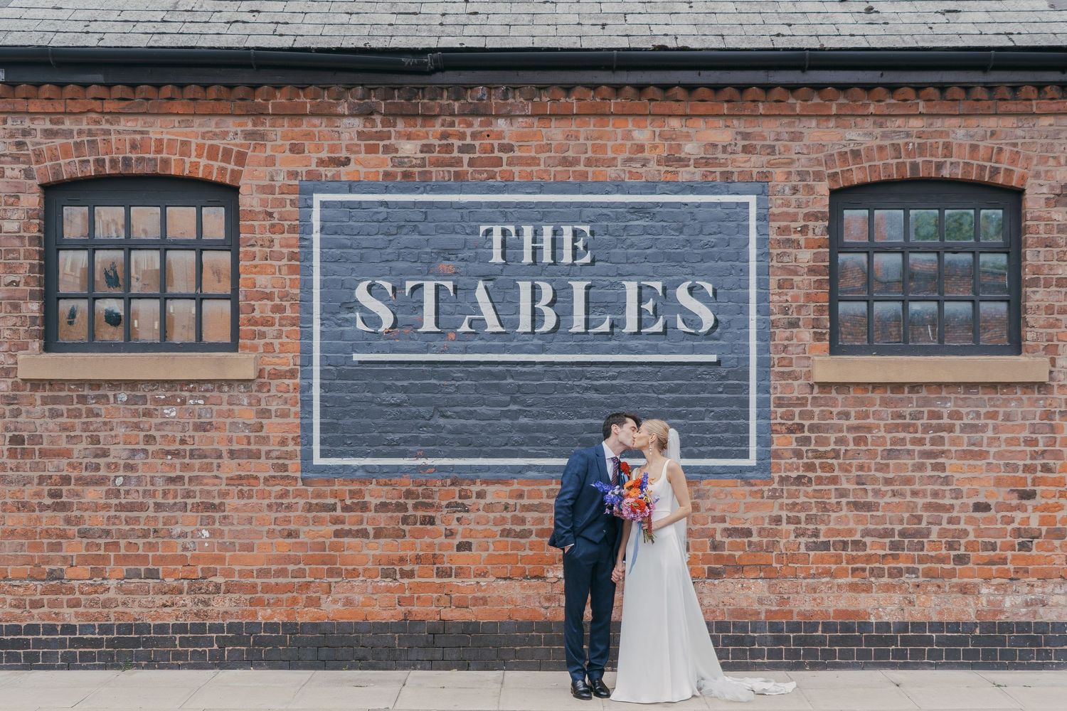 Historic brick building exterior with 'The Stables' signage and industrial-style windows.