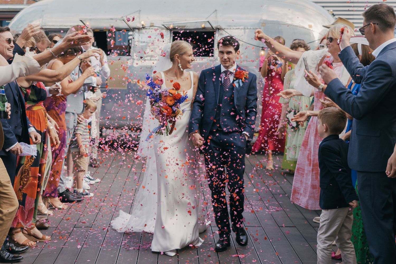 Wedding guests celebrate by throwing confetti at newlyweds exiting down brick steps in joyful ceremony moment.