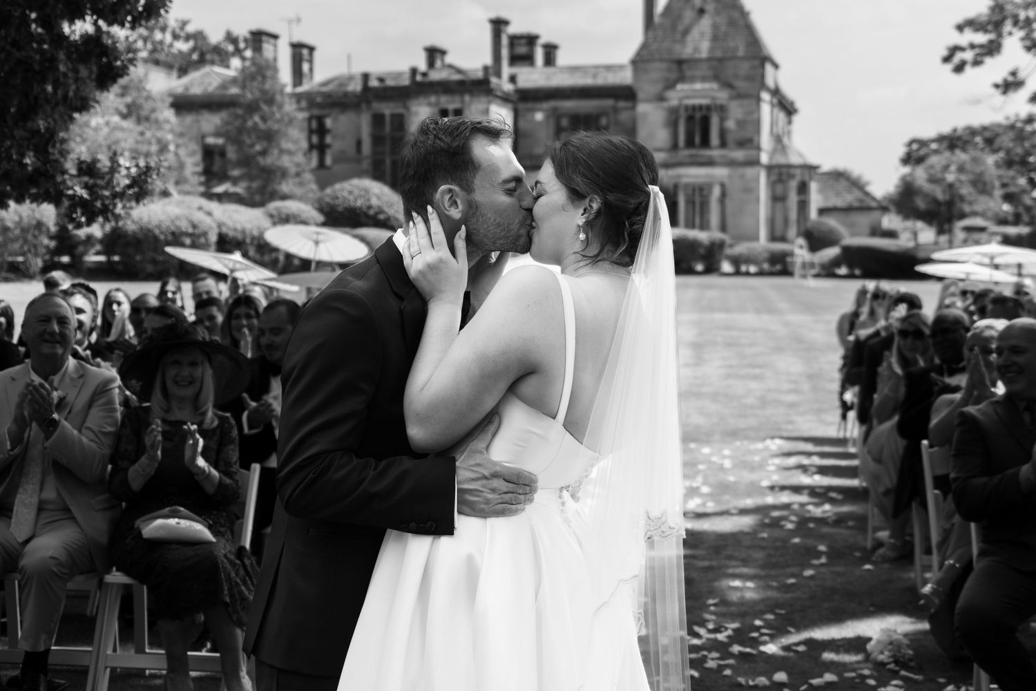Black and white outdoor wedding photo with historic mansion in background.
