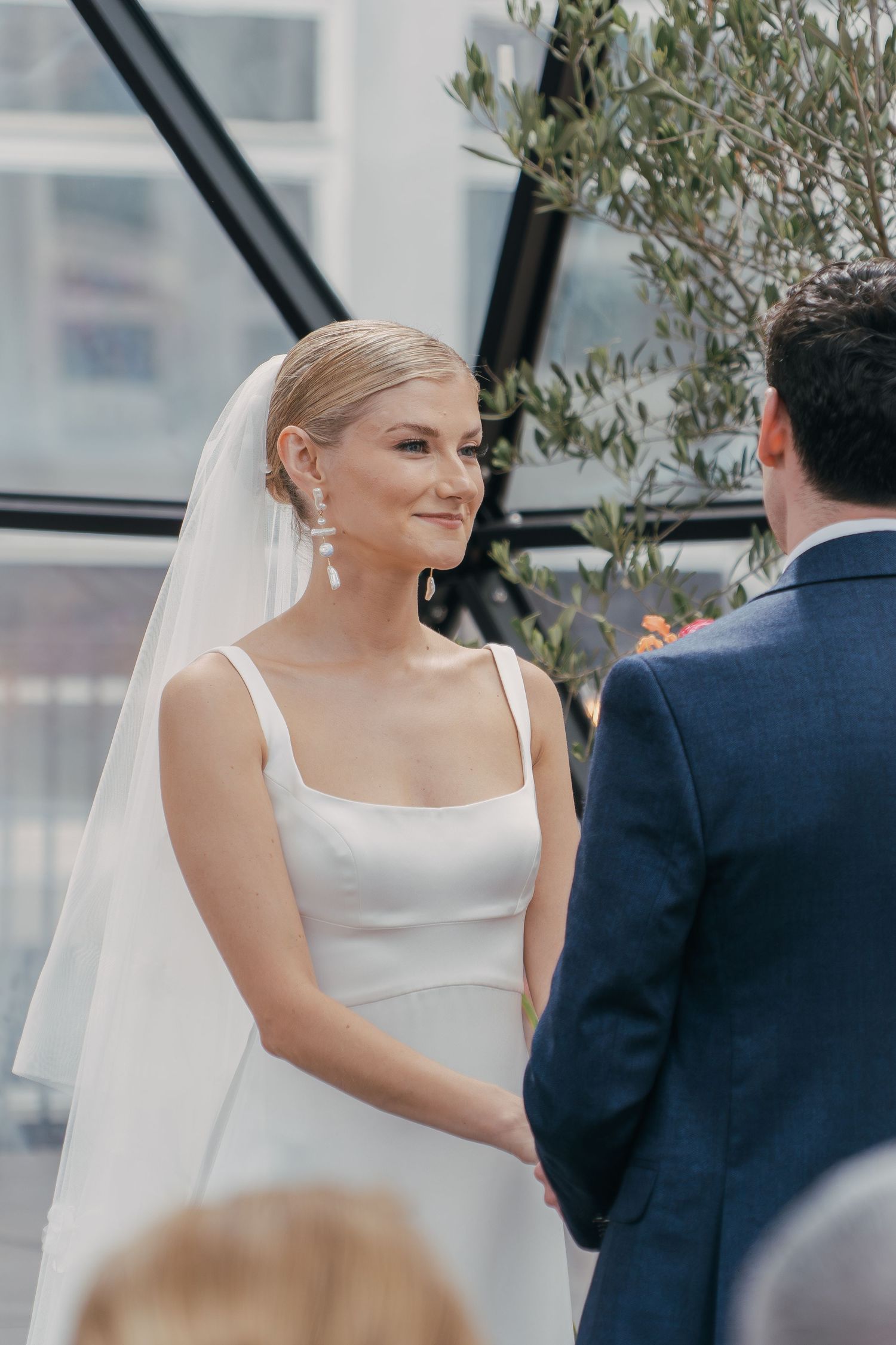 Elegant bride in white dress and veil speaks with groom during outdoor wedding ceremony.