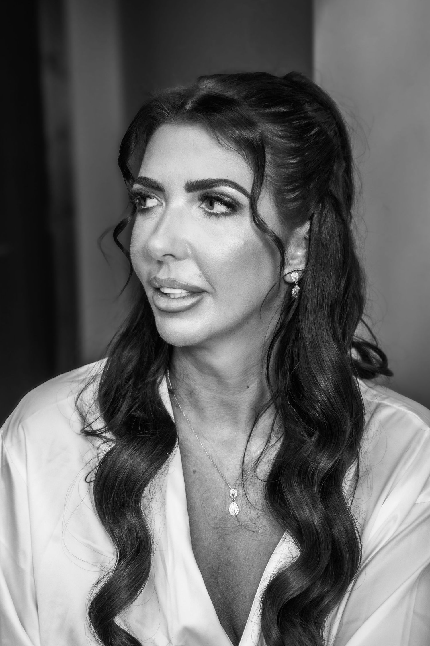 Black and white portrait of a woman with long dark wavy hair wearing a white button-up shirt and delicate jewelry.