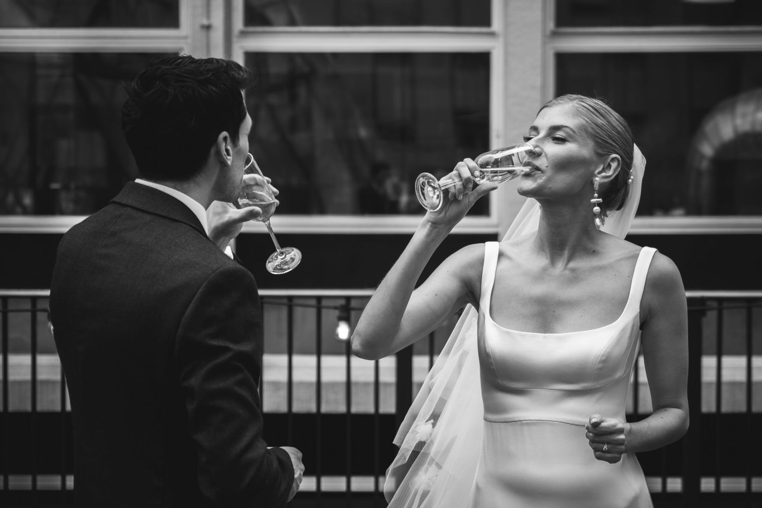 A bride and groom share a candid moment drinking champagne together in black and white photography.