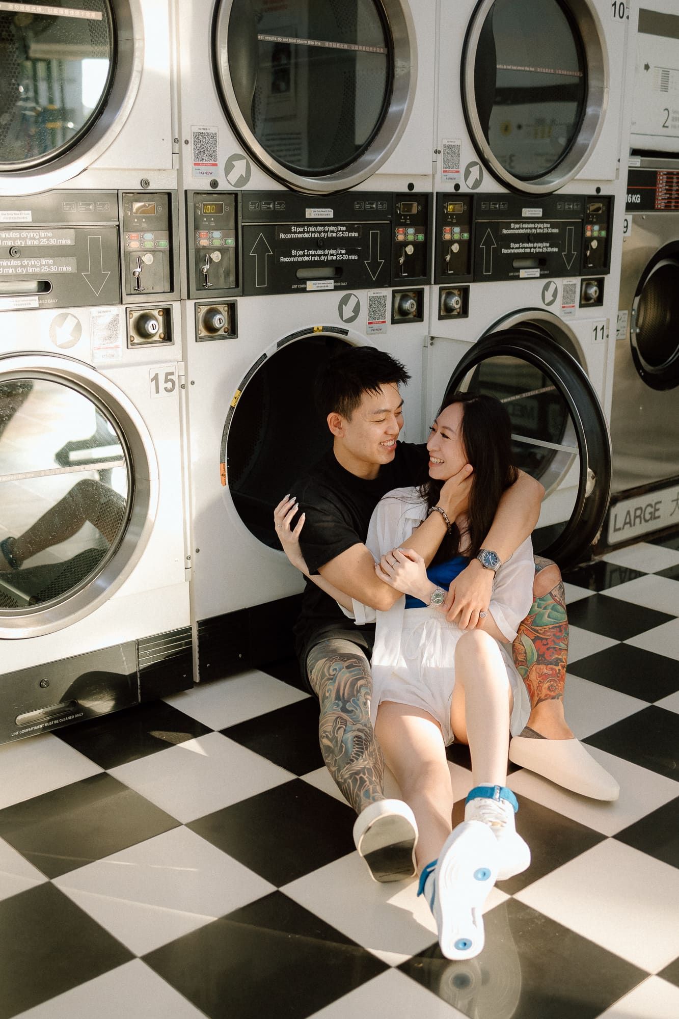 Couple shares intimate moments while sitting on the floor of a retro laundromat with vintage washing machines.