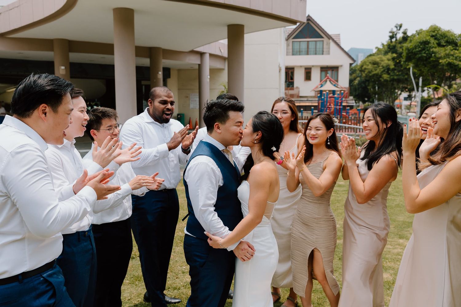 Wedding party celebrates joyfully in a garden setting with coordinated navy and blush attire.