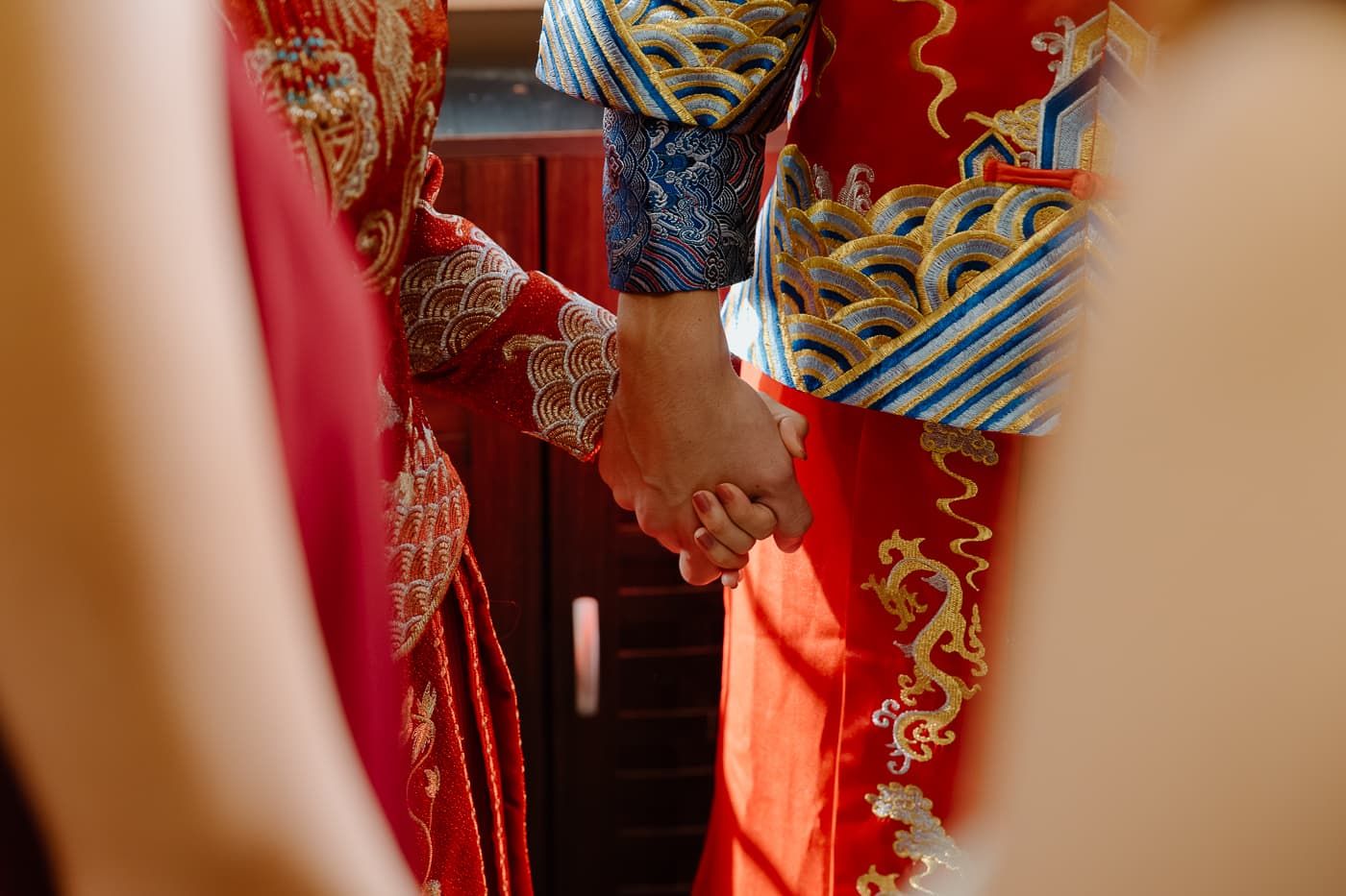 Close-up of hands in traditional Chinese wedding attire with intricate dragon embroidery.