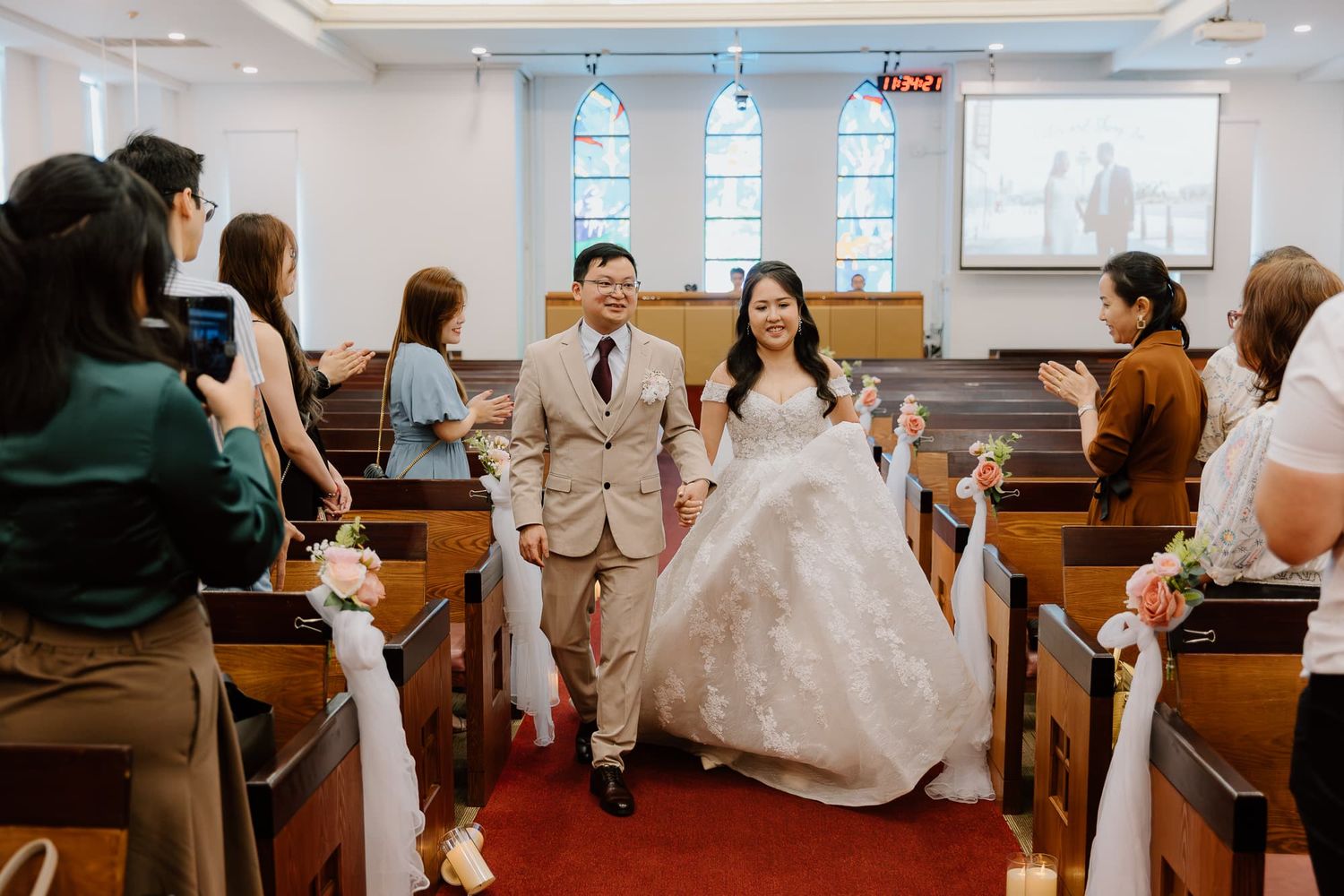 Wedding couple walks down church aisle decorated with white bows.