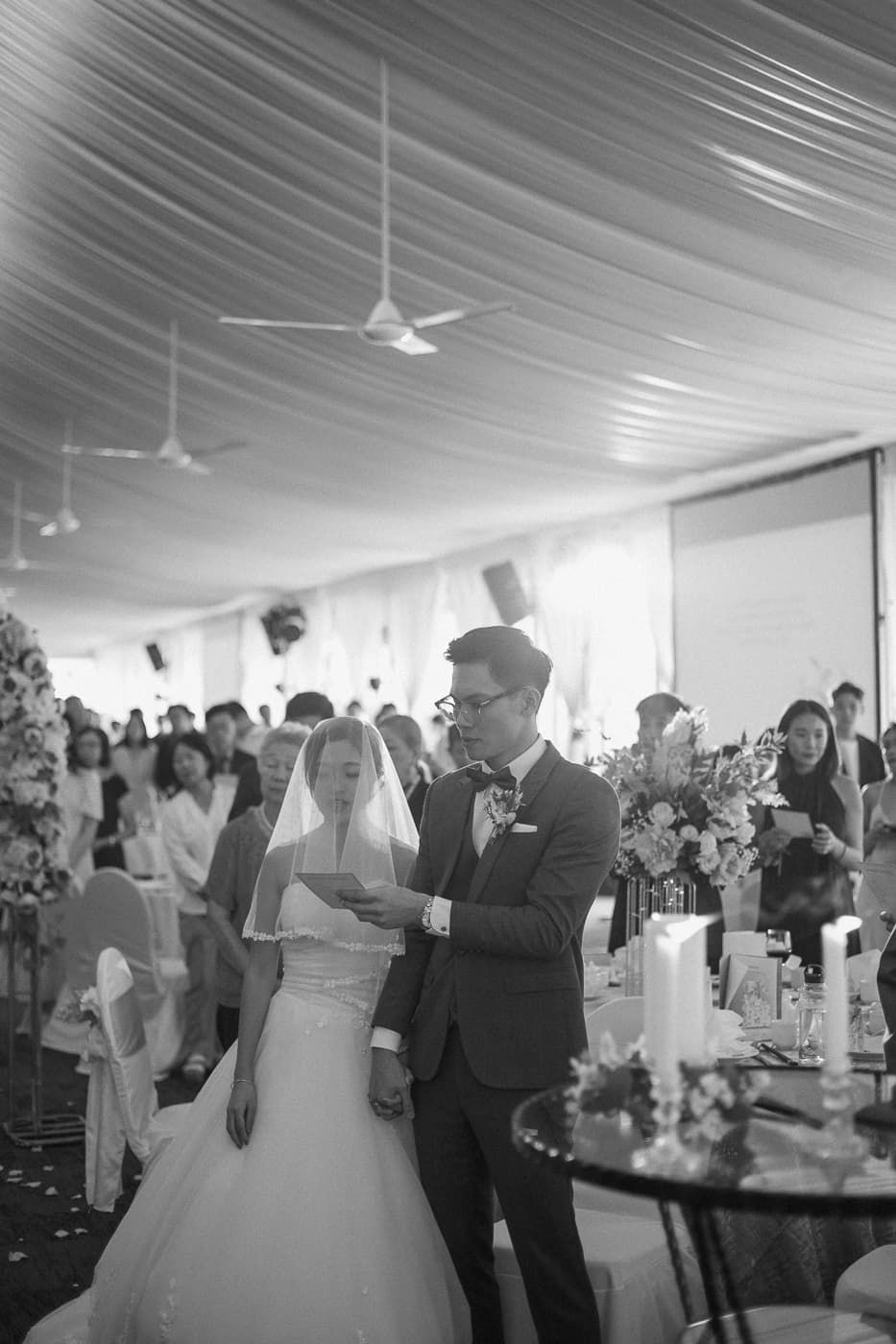 Black and white photo of wedding reception with guests and white tent ceiling.