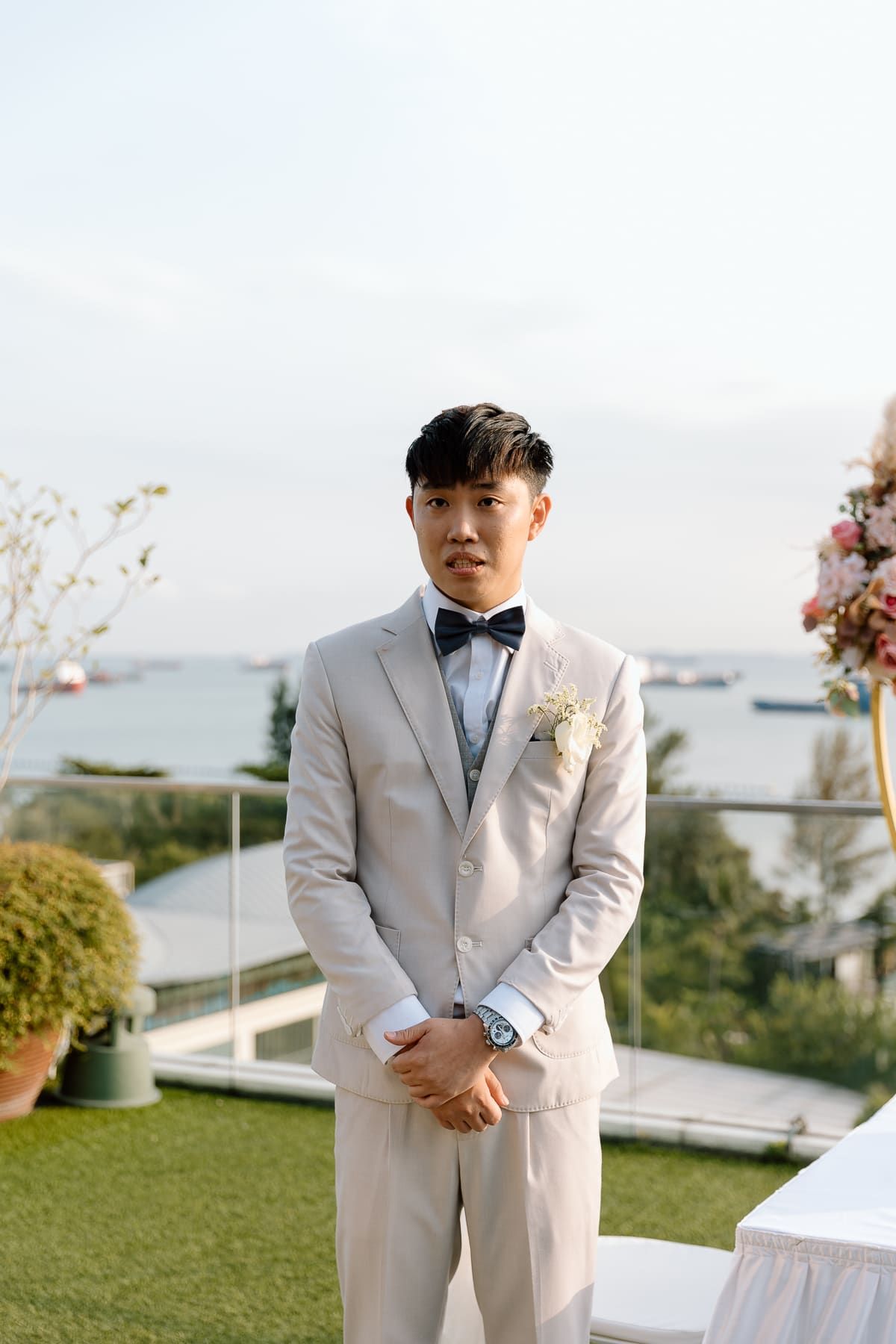 Person in light colored formal suit standing outdoors at scenic wedding venue.