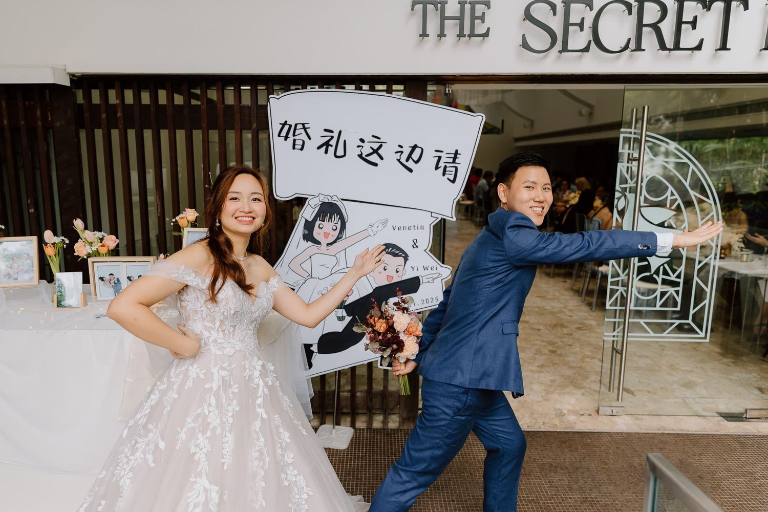 A couple poses playfully with signs outside a wedding venue entrance.