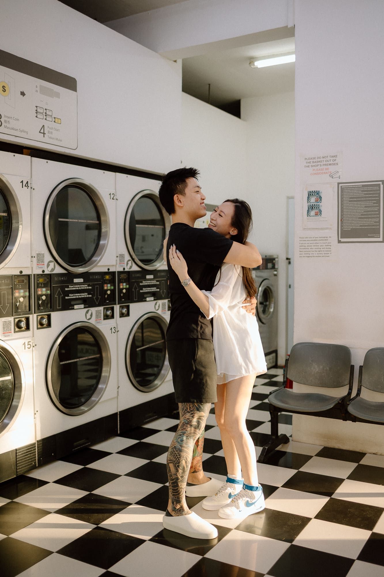 A romantic couple embraces and dances in a retro-style laundromat with black and white checkered floors.