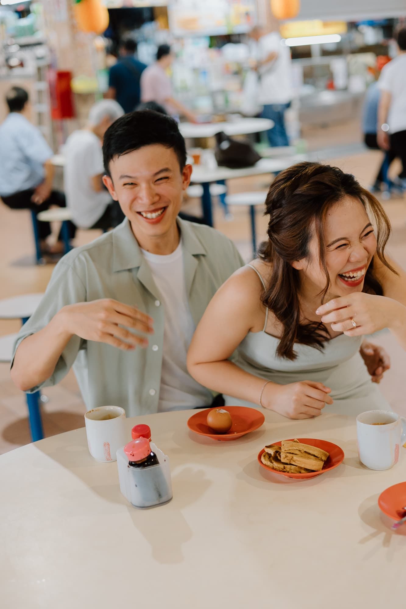A playful couple holding bread rolls against their cheeks while sitting at a restaurant table.