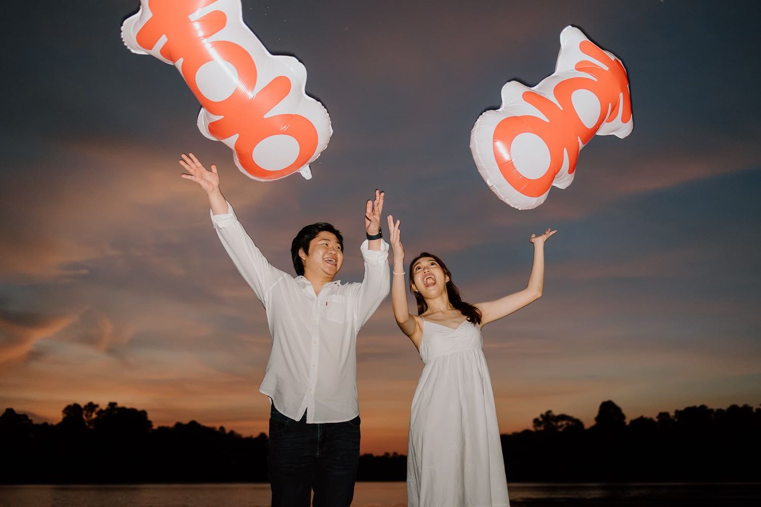 Two figures holding orange balloons against a dramatic sunset sky.