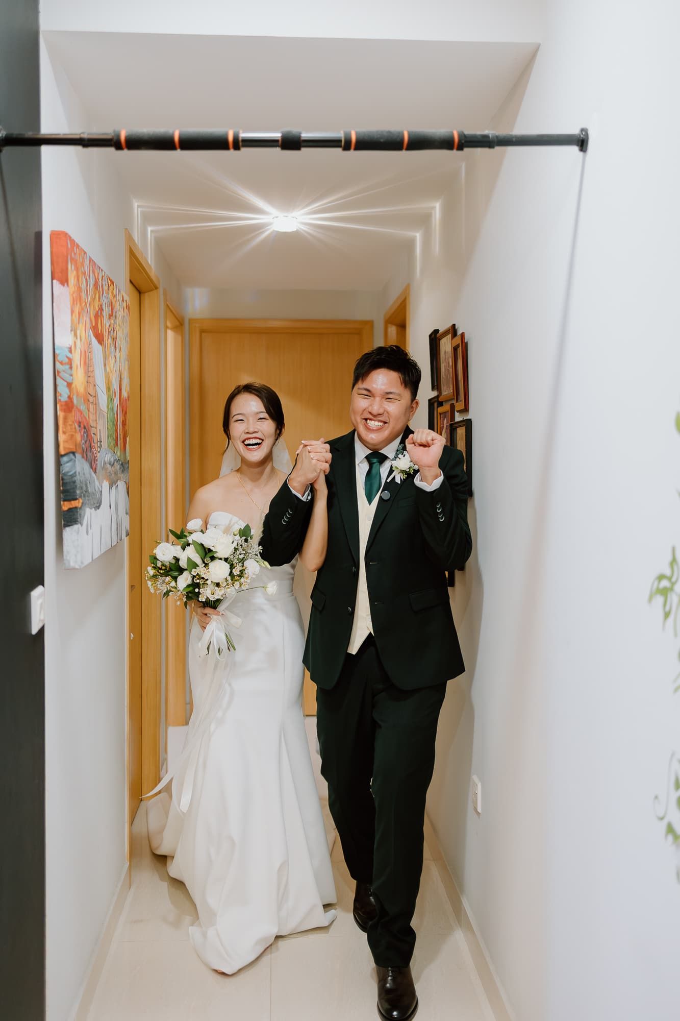 Joyful wedding couple celebrating in a bright hallway decorated with floral arrangements.