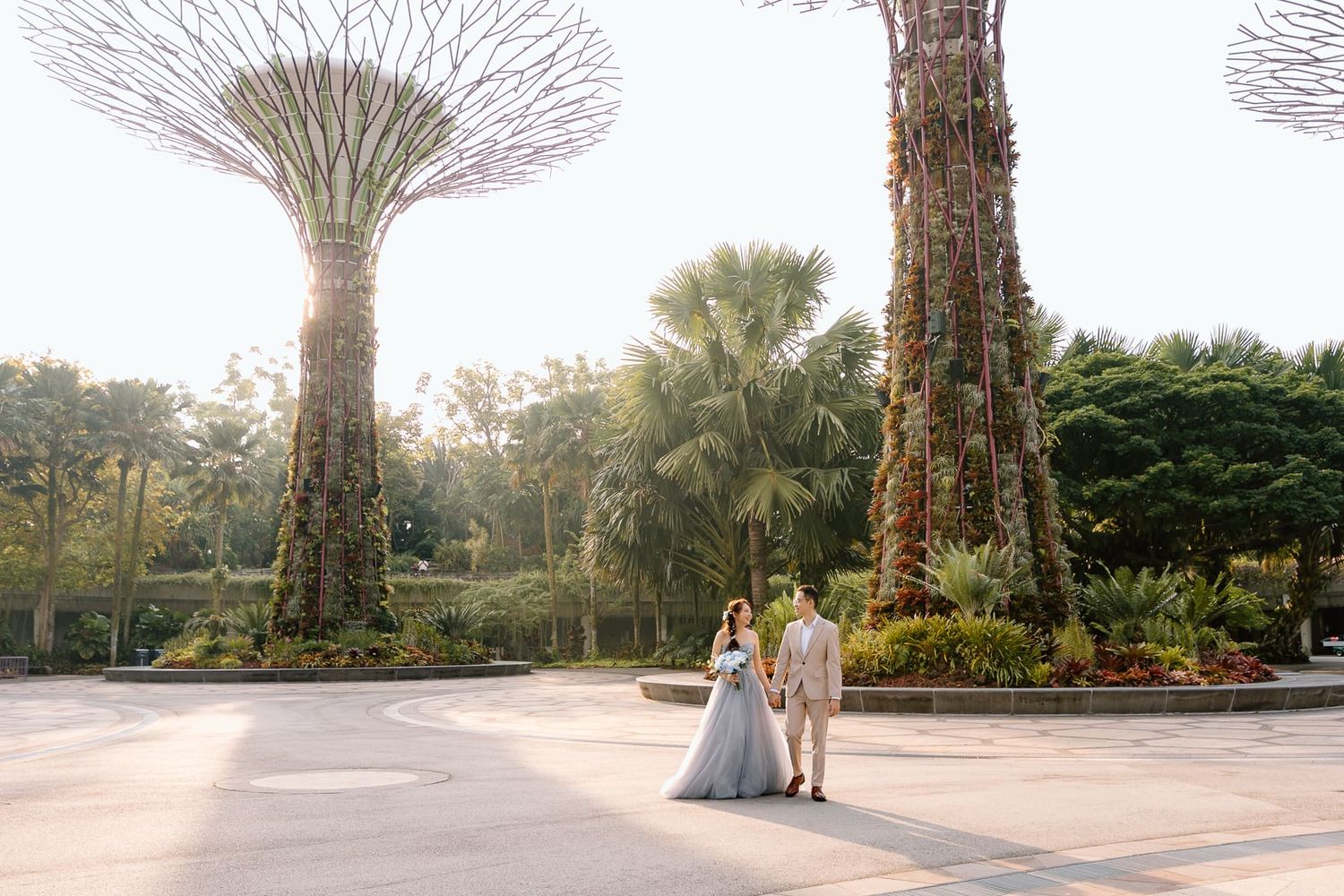 A wedding couple walking hand in hand beneath towering Supertrees at Gardens by the Bay.