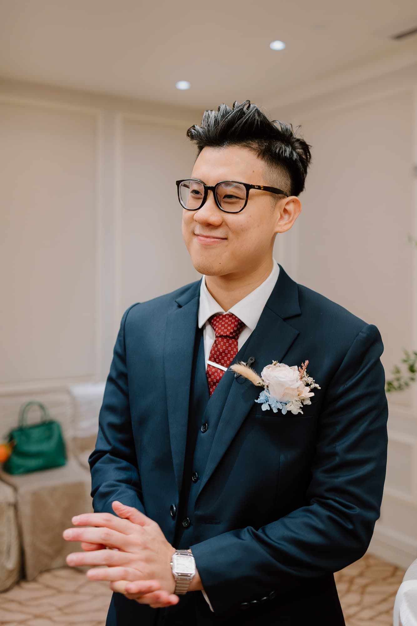 Formal attire with navy suit, red tie, and white boutonniere at a wedding.