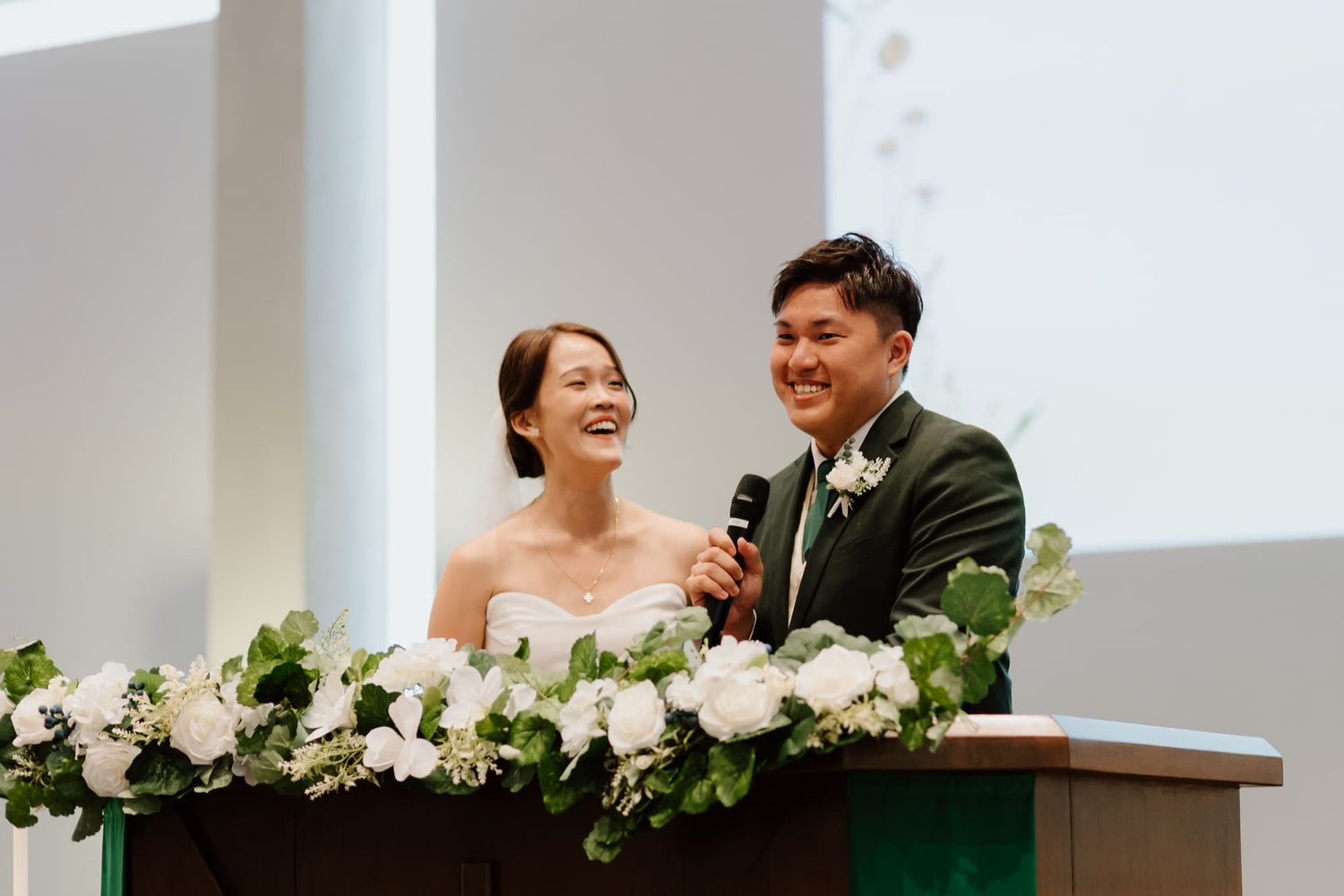 Wedding ceremony at a modern church altar decorated with white floral arrangements and greenery.
