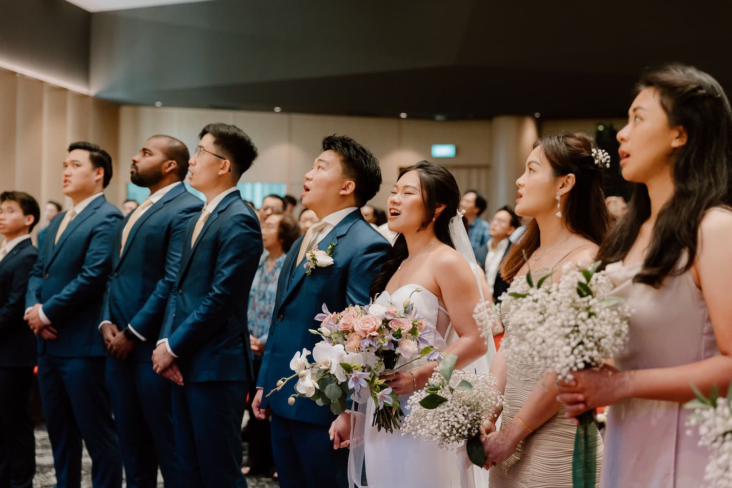Wedding party members stand in a line wearing navy suits and blush dresses.