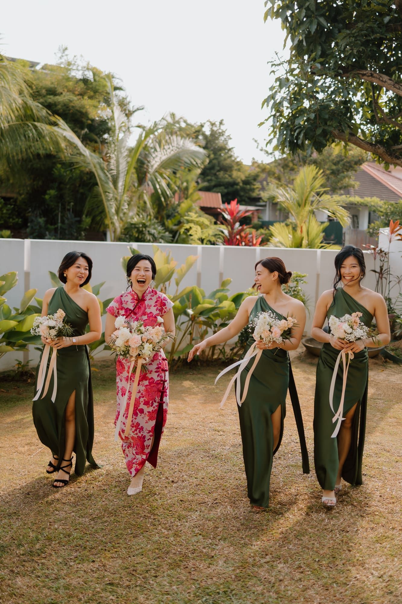 A group wearing traditional Hawaiian attire dances together in a line on grass with palm trees in the background.