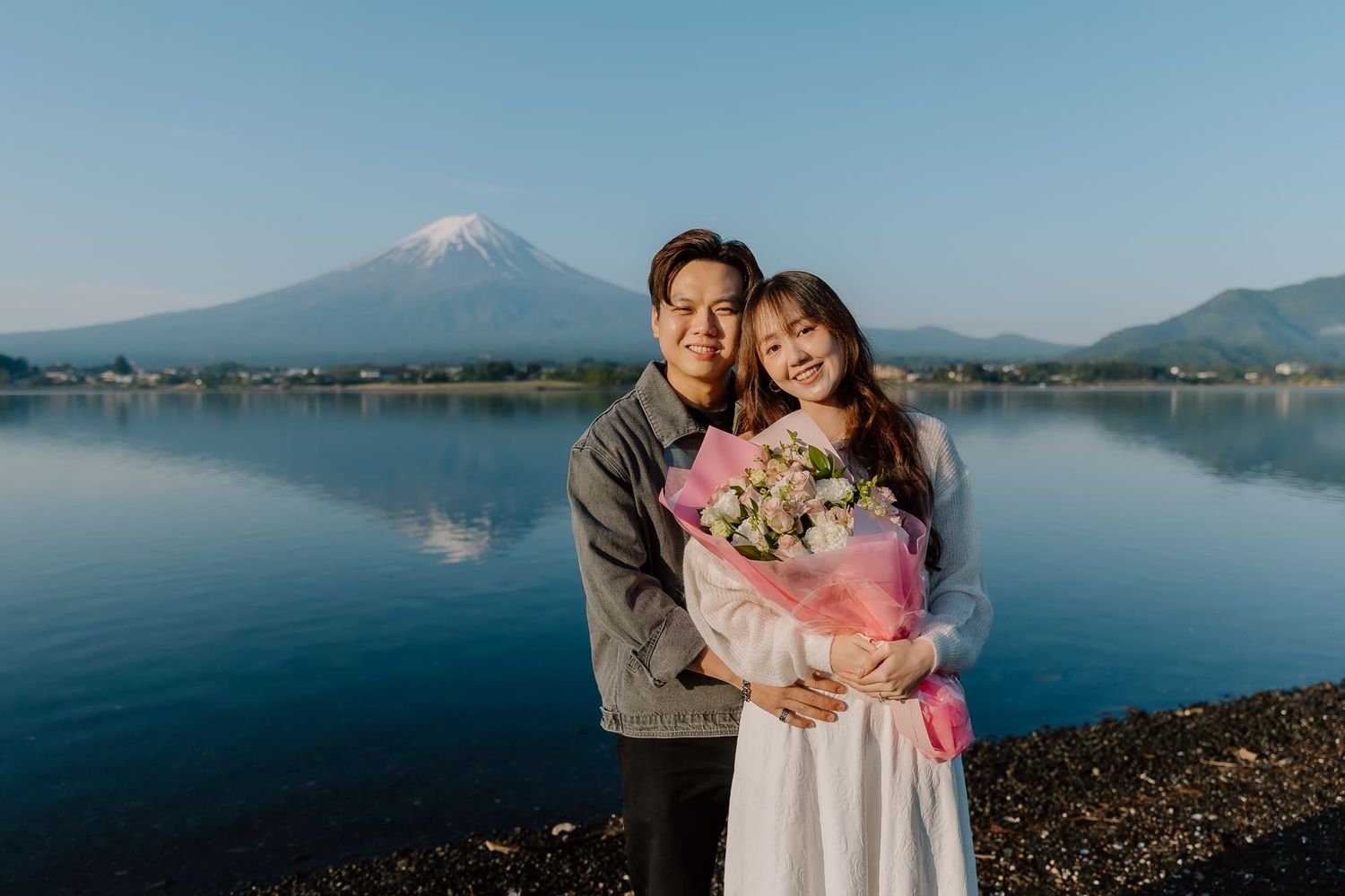 Couple embracing with flower bouquet at Lake Kawaguchiko with Mount Fuji in background, Japan.