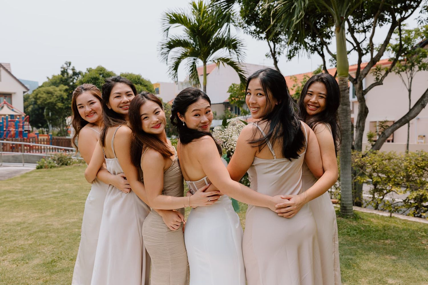 Bridesmaids in blush dresses embrace while laughing during wedding photo session.