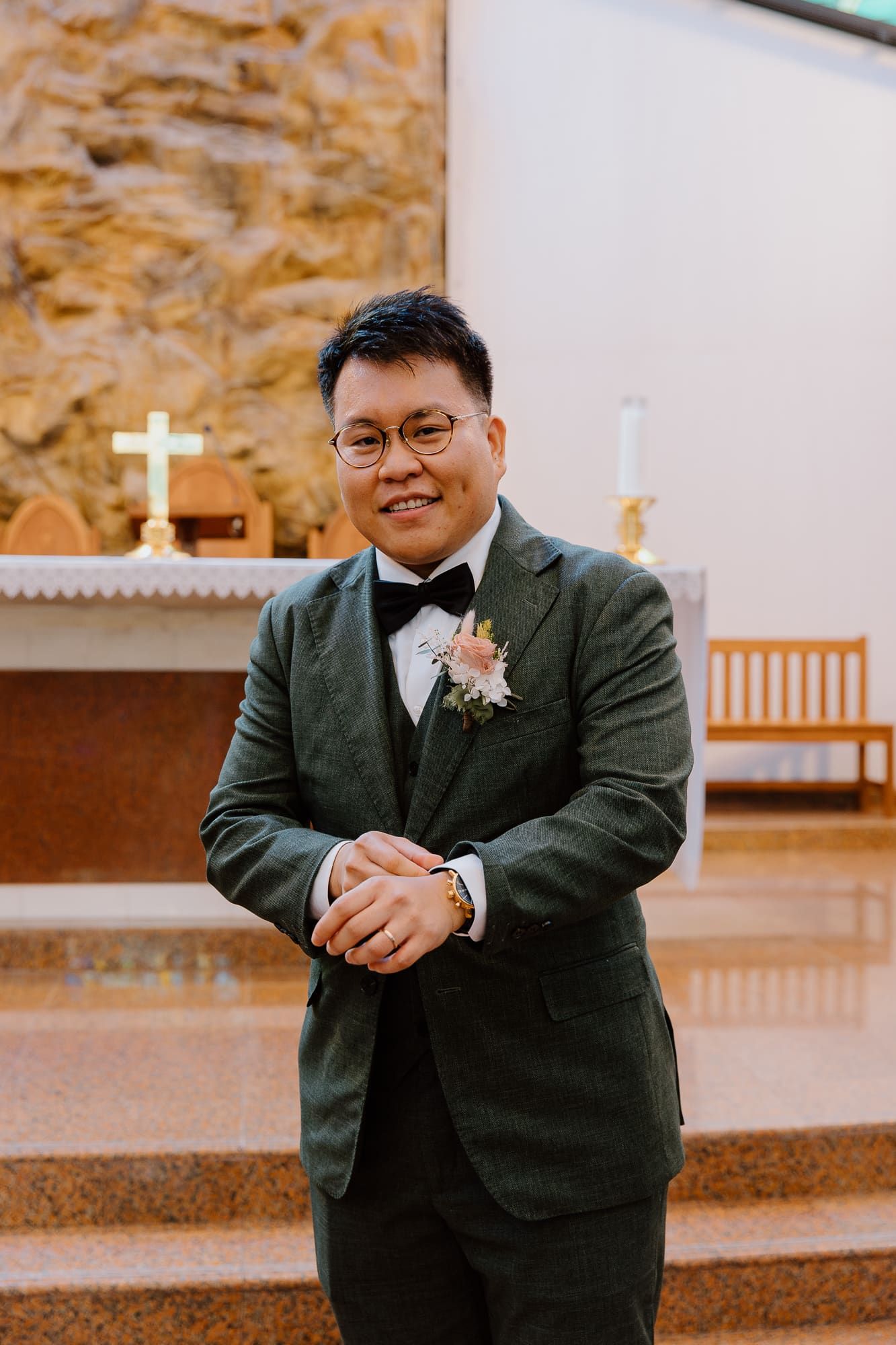 A wedding party member in a dark suit and boutonniere stands at the altar with joyful expressions.