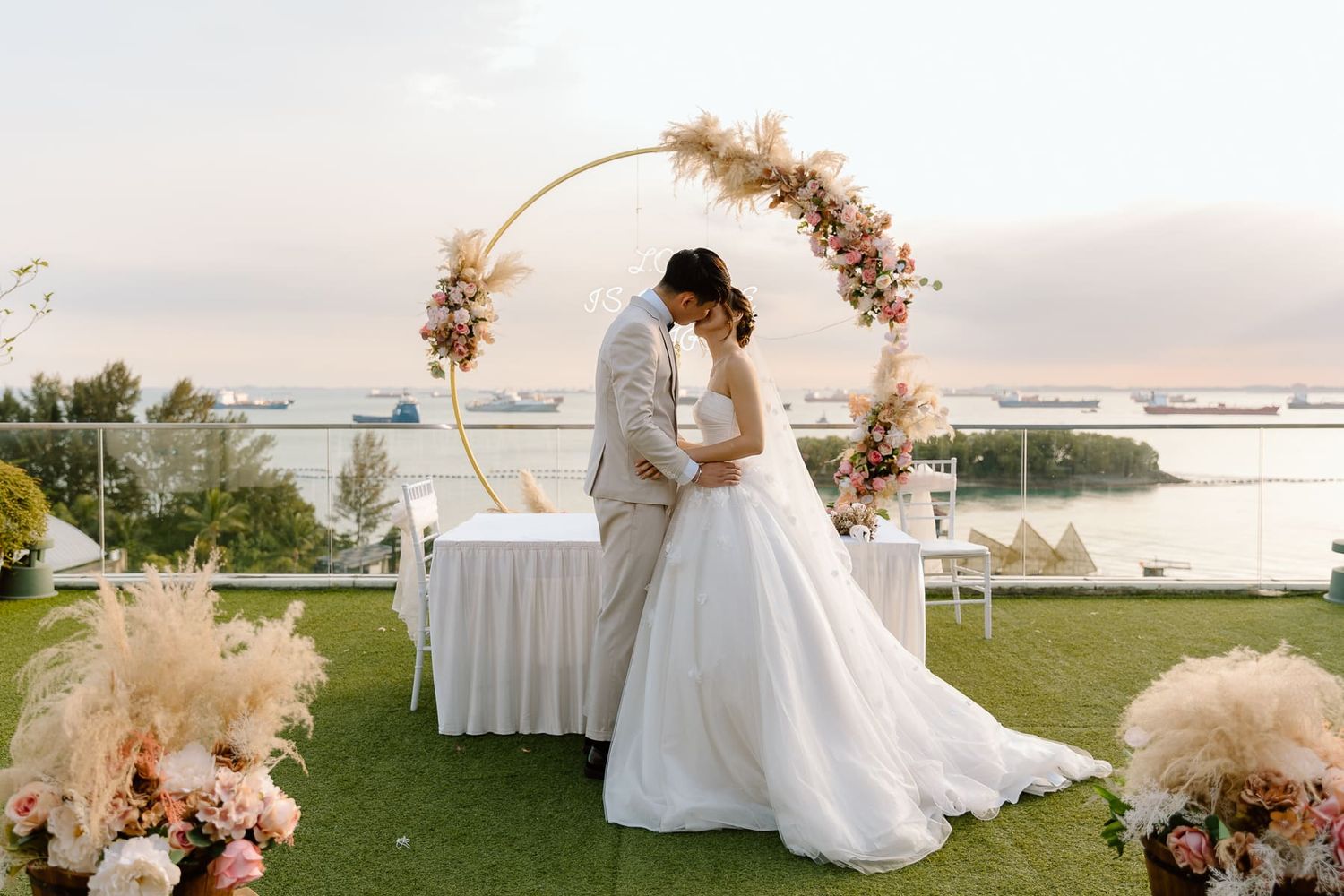 Elegant outdoor wedding setup with a circular floral arch and waterfront backdrop.