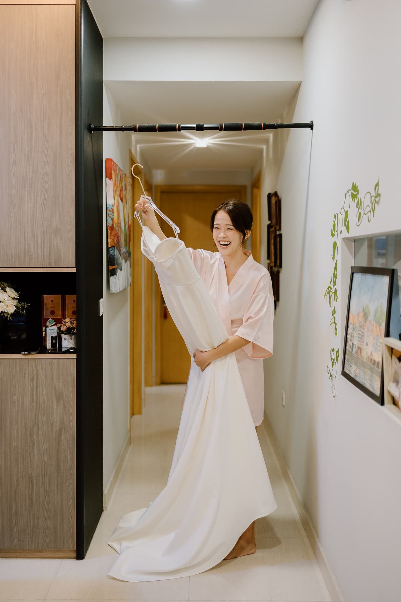 A joyful moment holding up a white wedding gown in a hallway.