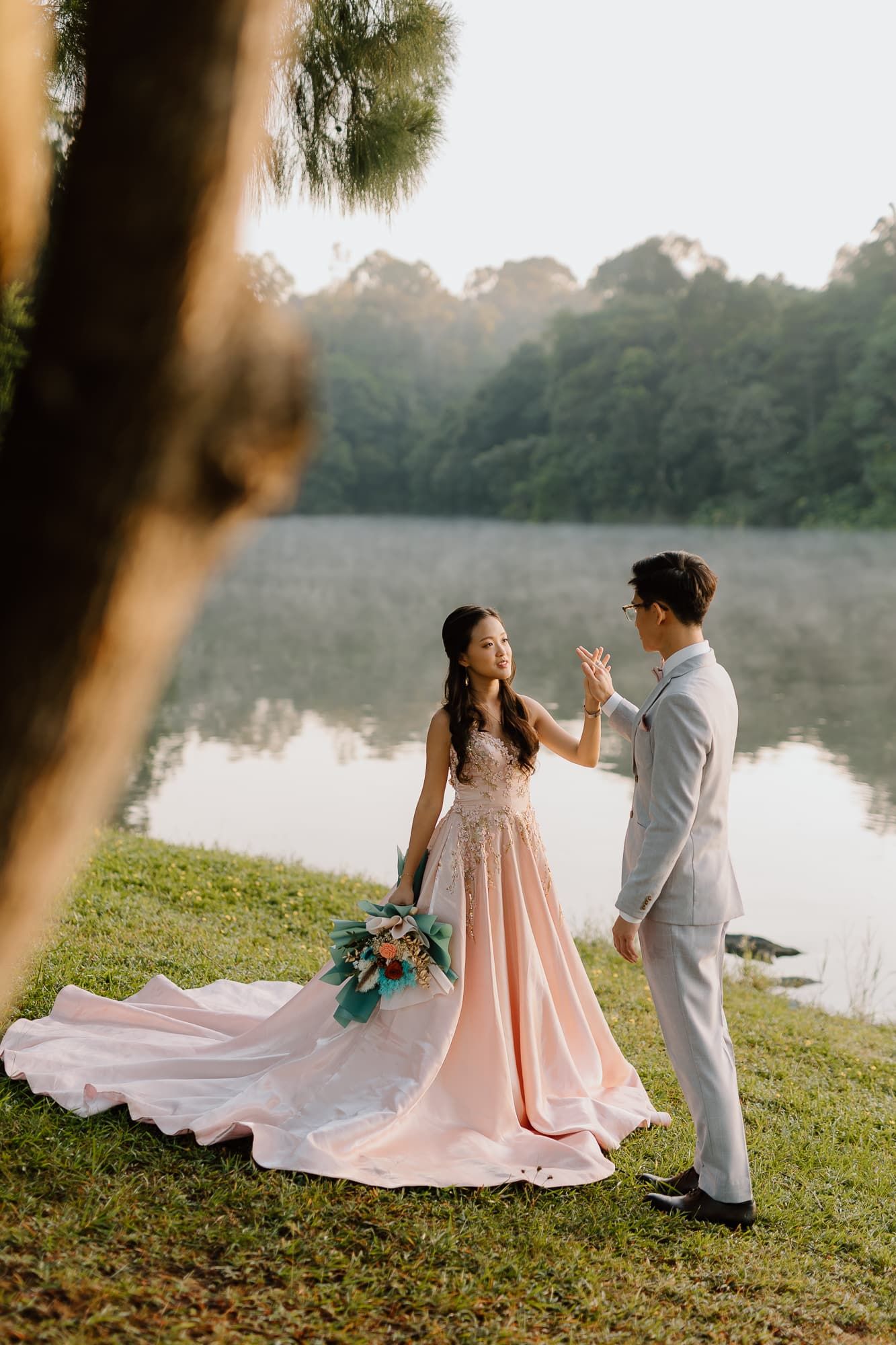 Romantic couple poses together during sunset photoshoot by a serene lake with pink dress flowing in the breeze.