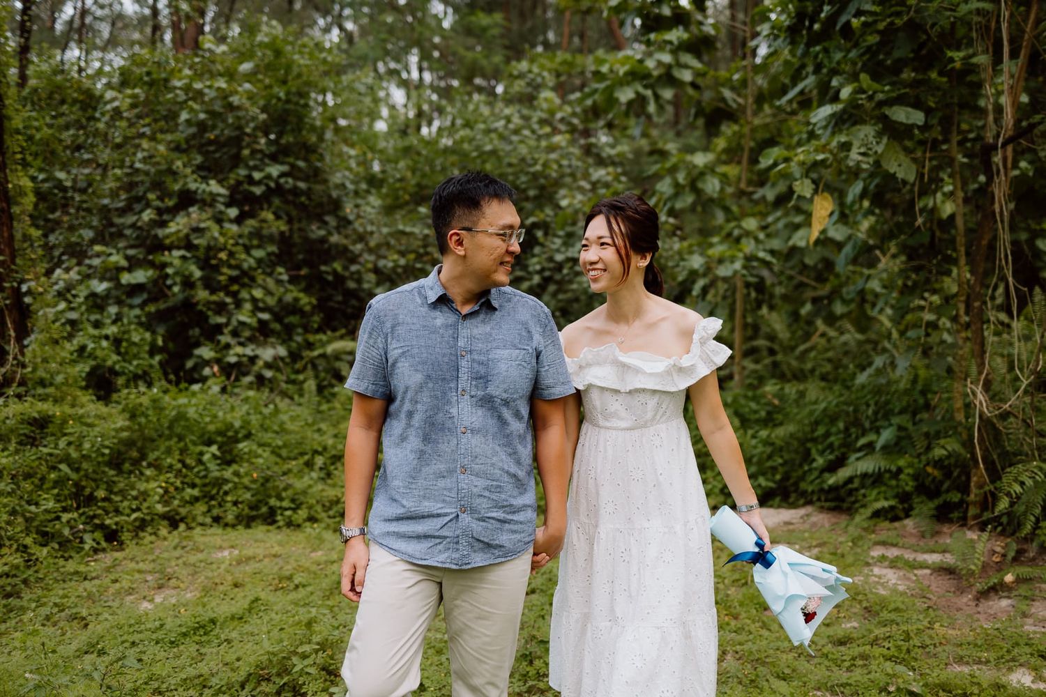 Couple walking together on a forest path in casual summer outfits.